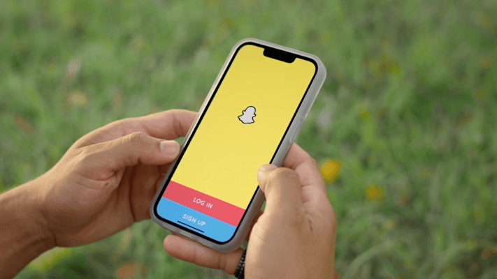Manos sostienen un móvil con la pantalla de inicio de sesión de Snapchat al aire libre
