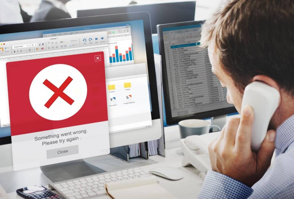 Hombre habla por teléfono frente a un monitor con un aviso de error en rojo