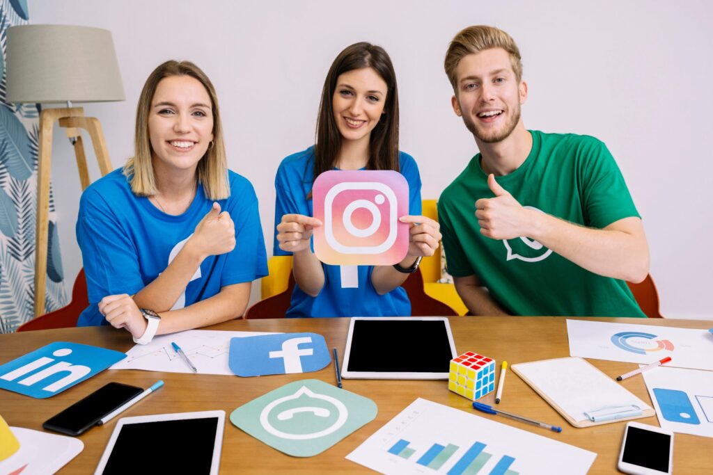 Three young people holding Instagram and WhatsApp icons at a table covered in social logos