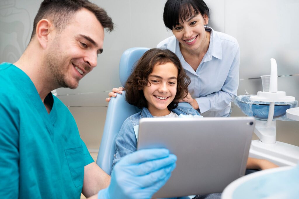 Odontólogo enseña una tableta a una niña acompañada de su madre en el sillón dental