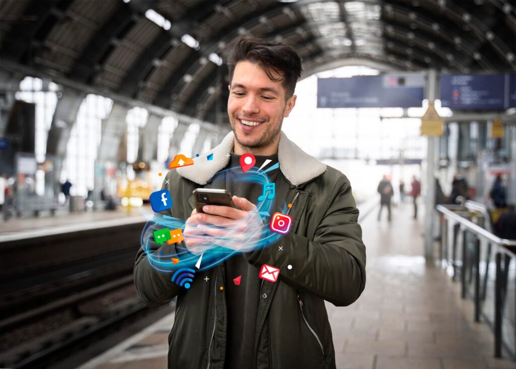 Man using his phone at a train station surrounded by social and messaging icons