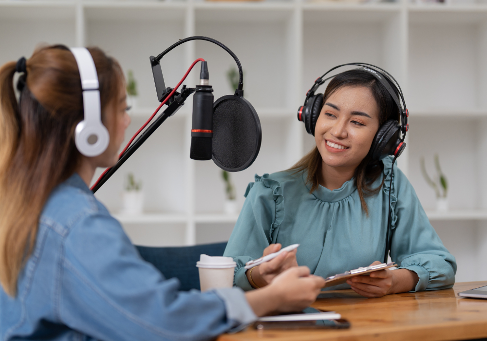 Dos mujeres graban un podcast con auriculares y micrófonos frente a una estantería