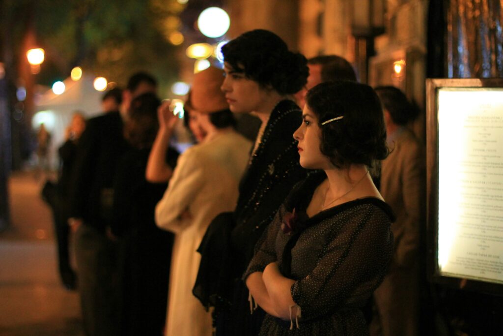 People in vintage clothing stand outside at night.