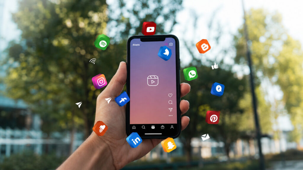 Manos sostienen un móvil del que salen los iconos flotantes de las principales redes sociales.