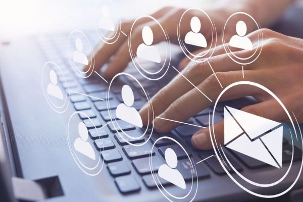 Manos teclean en un portátil mientras se superponen iconos de usuarios y de correo