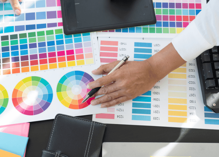 Manos trabajan con una tableta gráfica rodeadas de cartas de color y muestras impresas