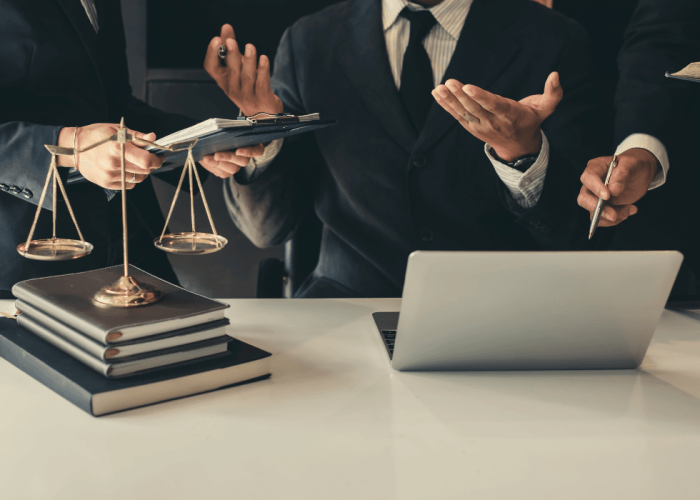 Abogados conversan en una mesa con una balanza de la justicia, libros y un portátil