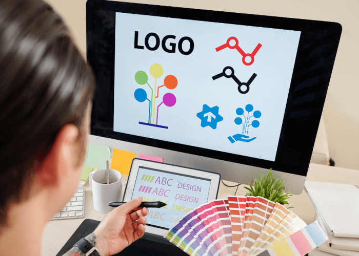 Diseñadora revisa propuestas de logotipo en un monitor con un abanico de muestras de color