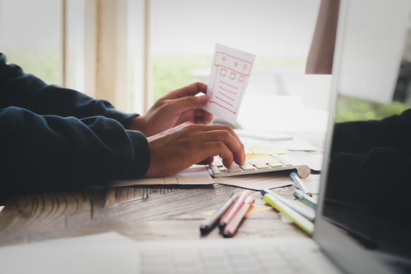 Persona teclea en un portátil sobre un escritorio con documentos y material de oficina